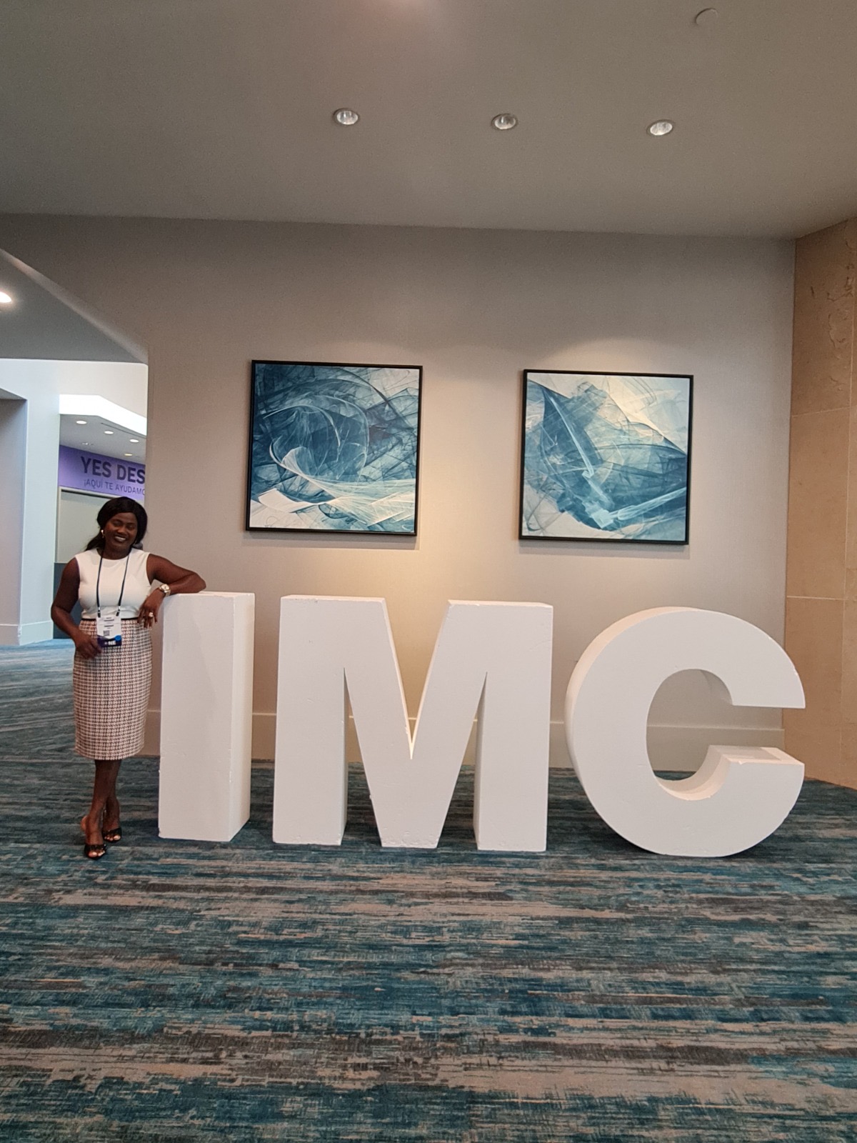 Kemi Areola beside the IMC letters at the International Maxwell Conference